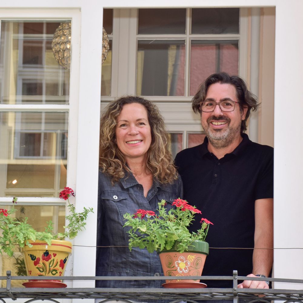 Lächelnde Geschäftsführer am geöffneten Fenster mit blumengeschmücktem Geländer