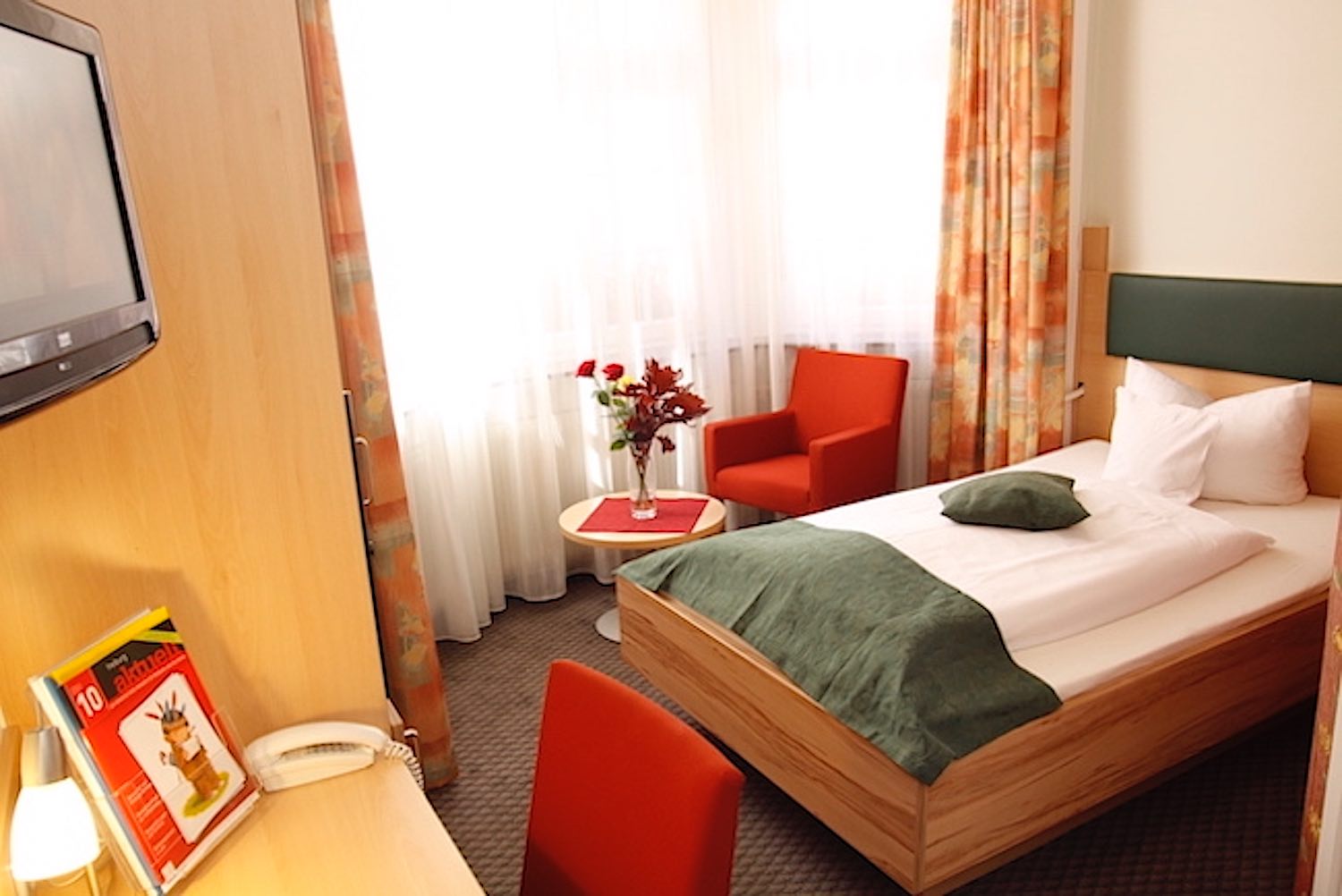 Beleuchtetes Einzelzimmer mit Fernseher, Sesseln und Schreibtisch
