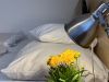 Blumen auf dem Nachttisch, Doppelbett mit großen und kleinen Kissen