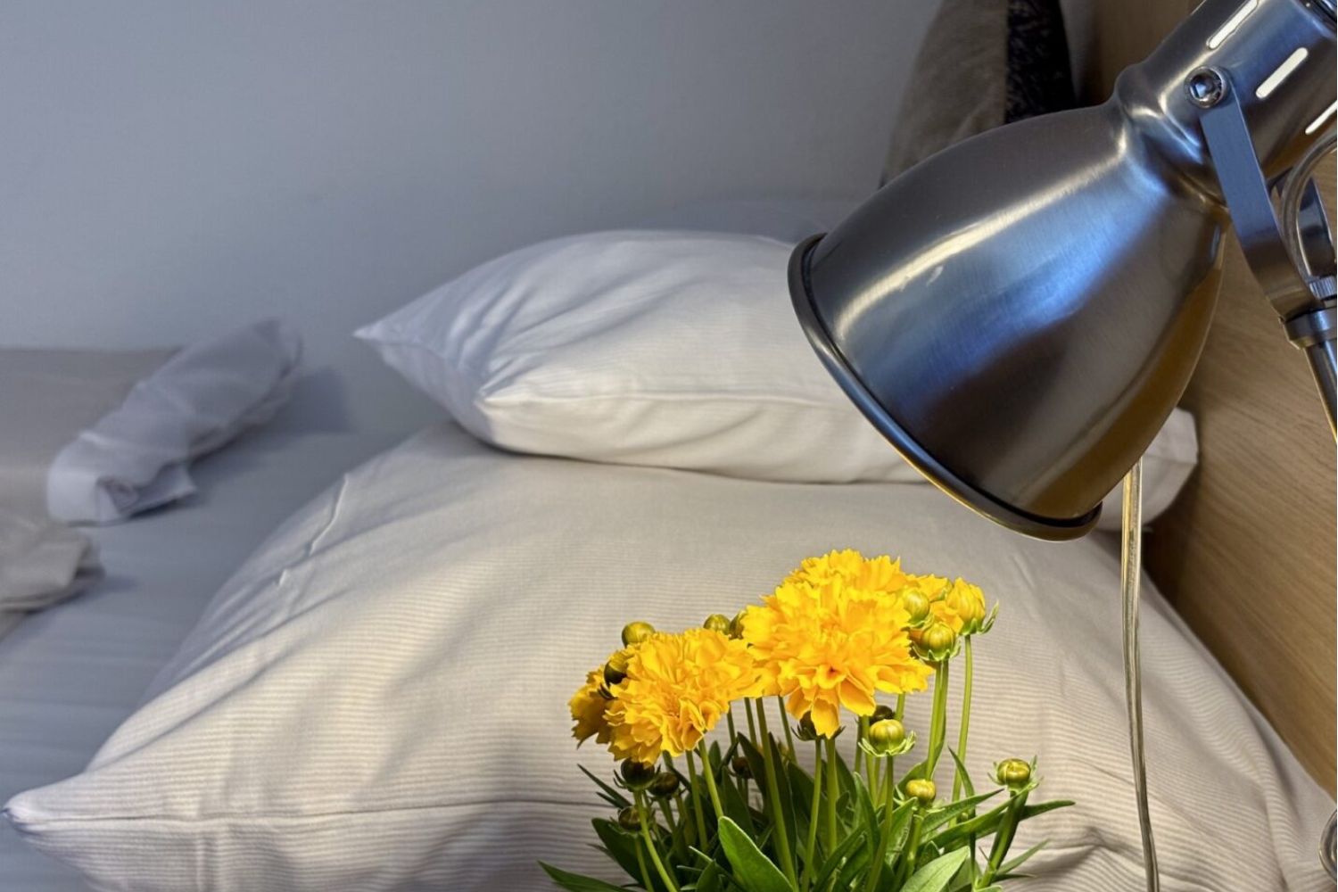 Blumen auf dem Nachttisch, Doppelbett mit großen und kleinen Kissen